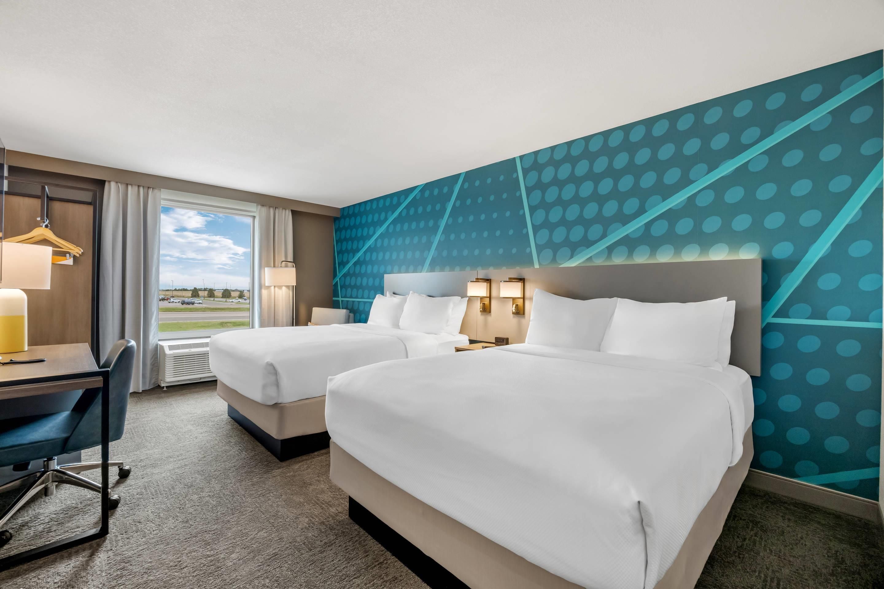 A hotel room with two beds, a desk, and a view of the outside.