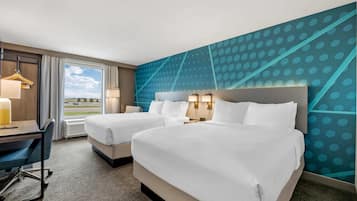 A hotel room with two beds, a desk, and a view of the outside.