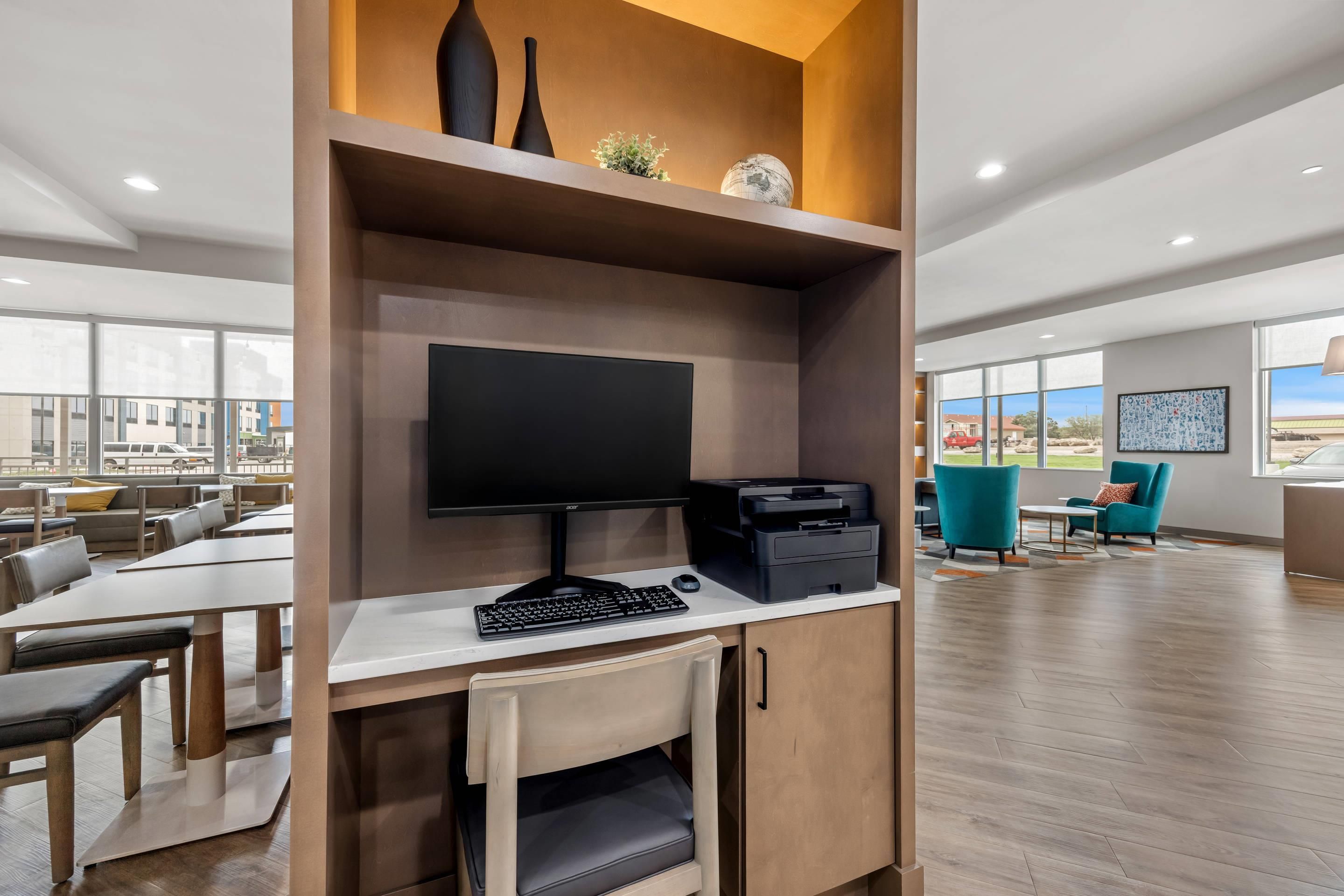 A modern office space with a desk, computer, printer, and a view of the outside.