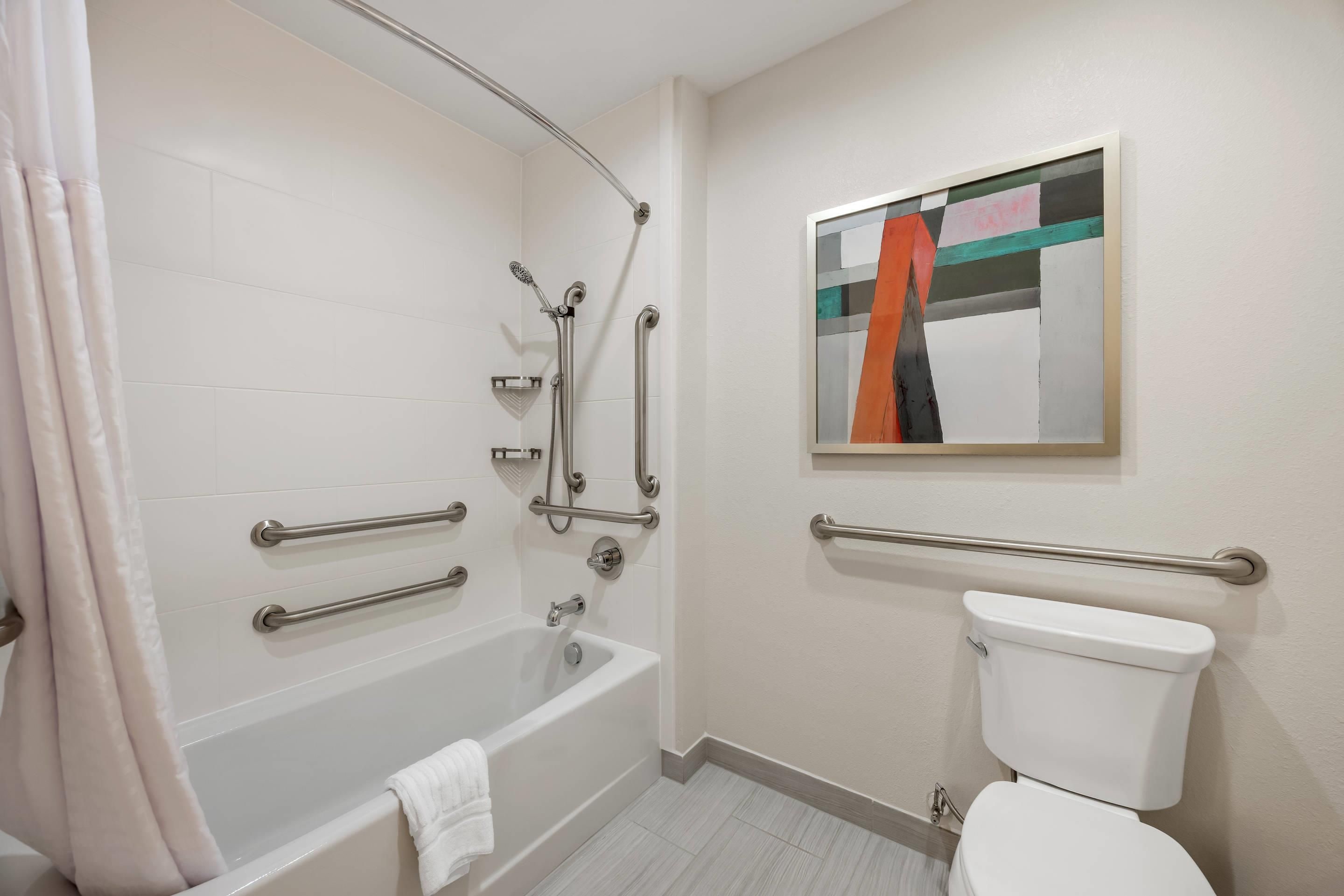 Un baño con bañera, inodoro y barras de apoyo.