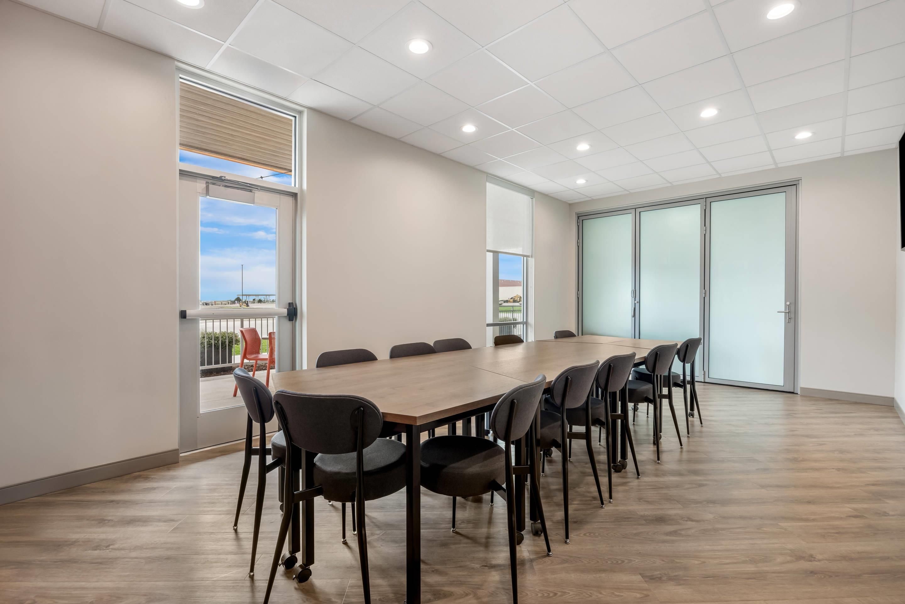 A conference room with a long table and chairs, large windows, and a view of the outdoors.