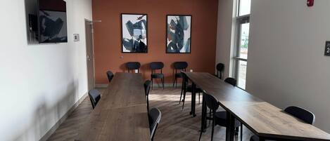 Un salón de conferencias con una larga mesa de madera, sillas negras y dos cuadros abstractos en la pared.