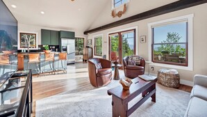 A spacious living room with a large window, a ceiling fan, and a wooden bench. - Idaho Springs Dream Cabin – Cozy Seclusion with Gorgeous Mountain Backdrop (Idaho Springs)