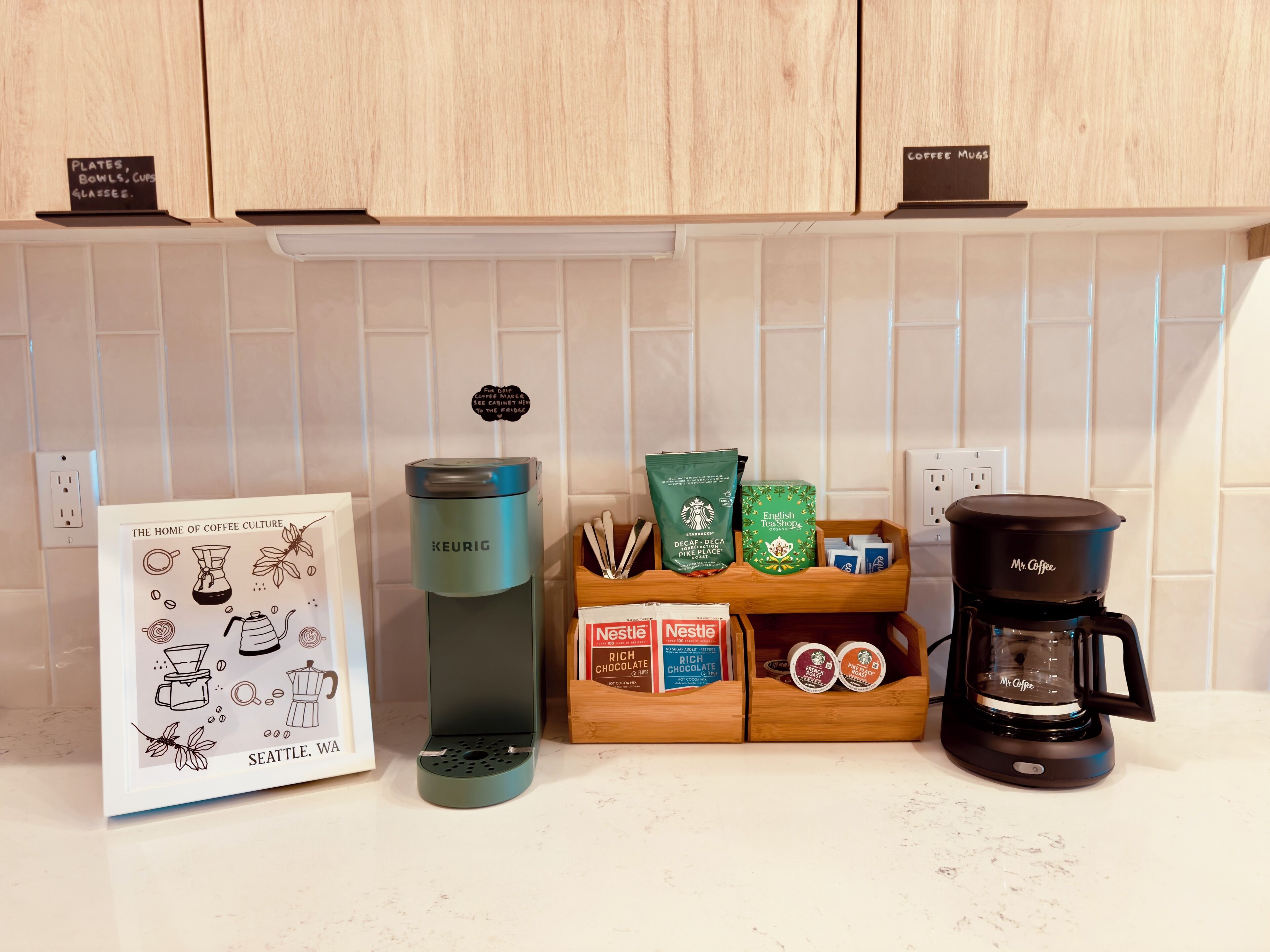 Un comptoir de cuisine avec une machine à café Keurig, une autre machine à café de la marque Mr. Coffee, et un support pour dosettes de café contenant des dosettes Starbucks et Nestlé.