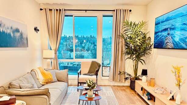 Een moderne woonkamer met een bank, fauteuil, salontafel en een groot raam met uitzicht op de stad.