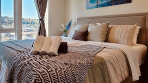 Een slaapkamer met een groot bed, uitzicht op de stad en een schilderij van golven aan de muur.