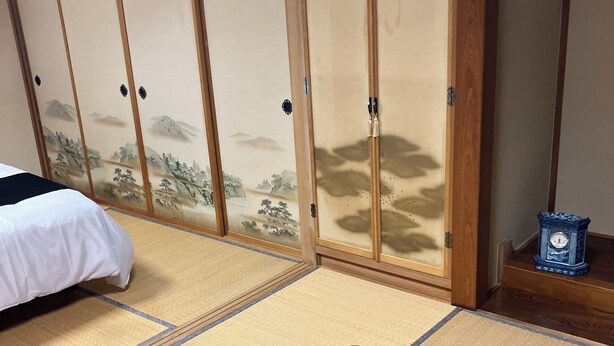 A traditional Japanese room with tatami flooring, a low wooden bed, and sliding shoji doors with a mountain landscape design.