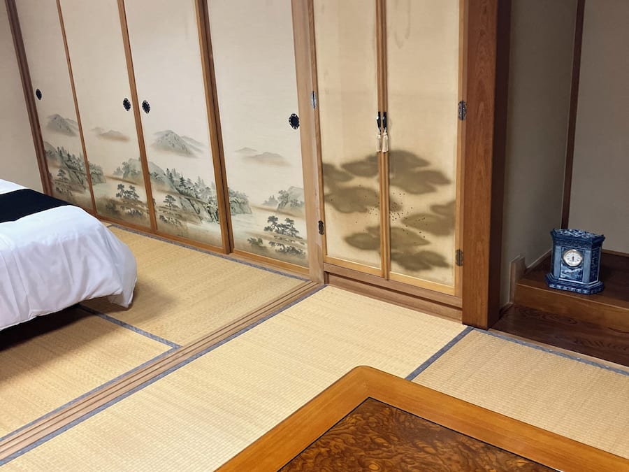 A traditional Japanese room with tatami flooring, a low wooden bed, and sliding shoji doors with a mountain landscape design.