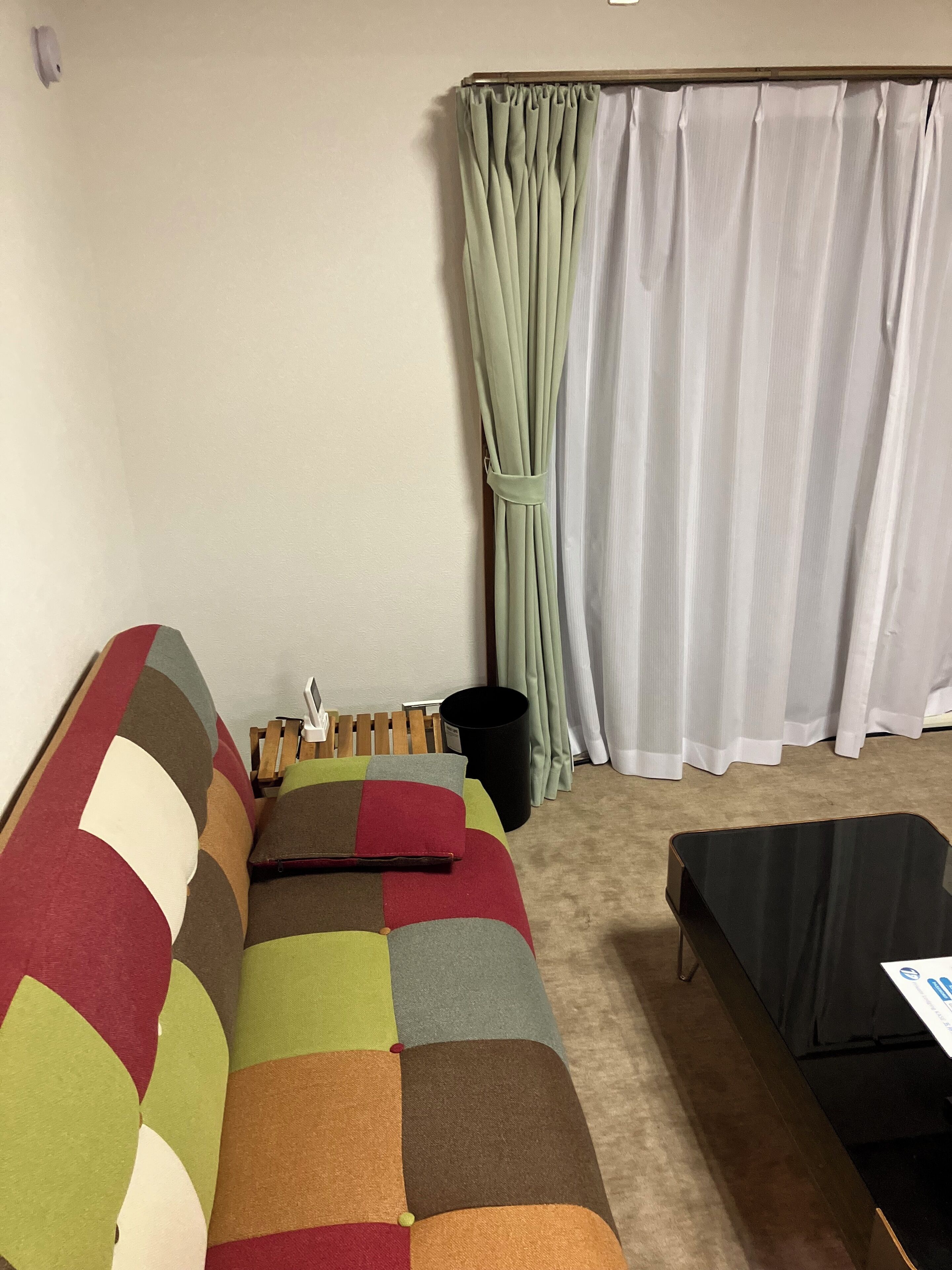 A room with a colorful sofa, a small table, and a window with curtains.