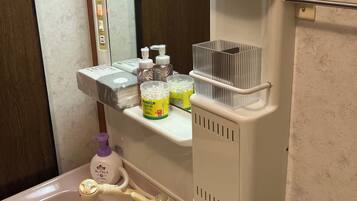 Un baño con lavamanos, espejo y repisas con artículos de aseo.