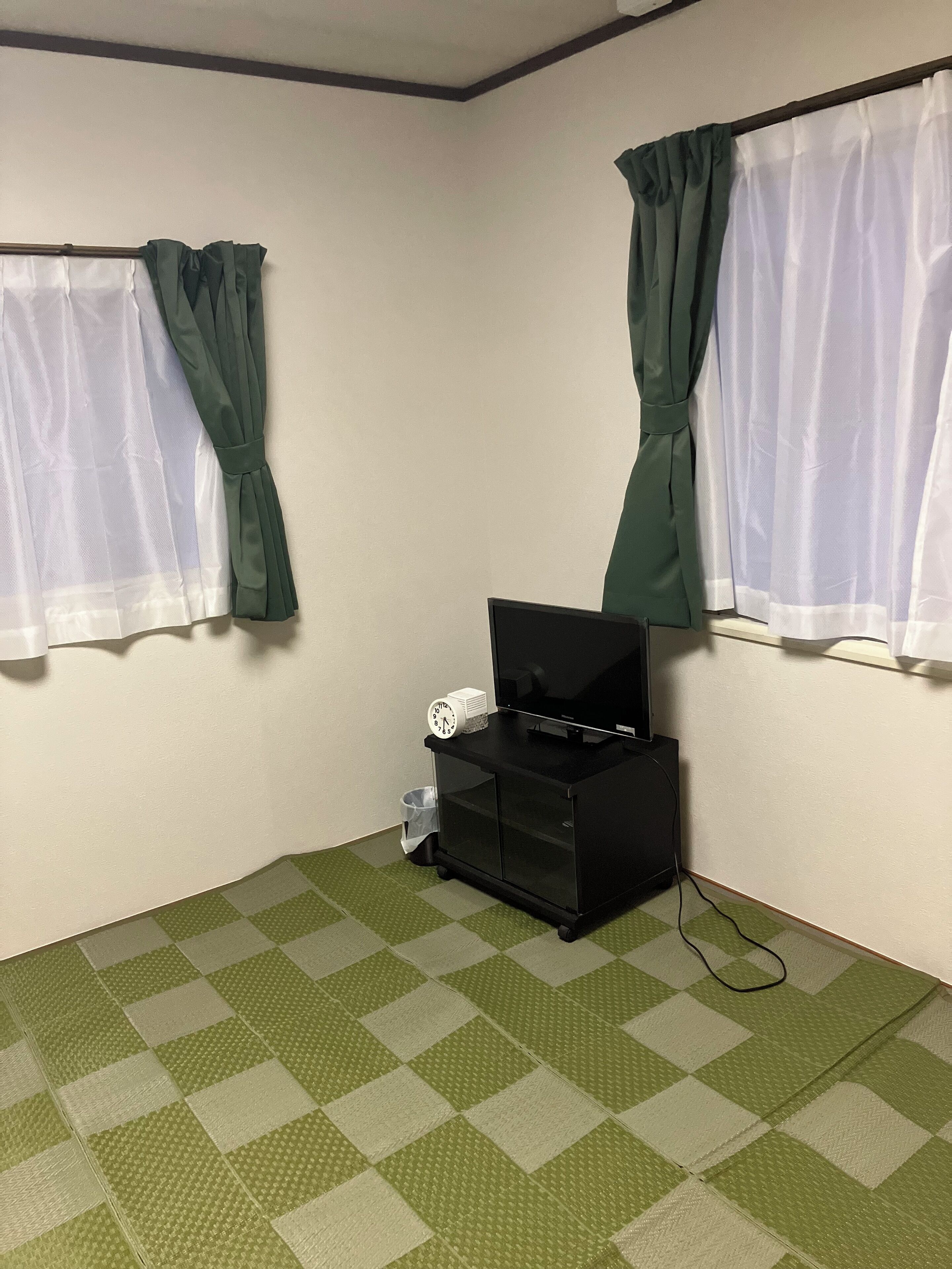 Een kamer met een geruite vloer, een zwart tv-meubel met een klok, en gordijnen voor de ramen.