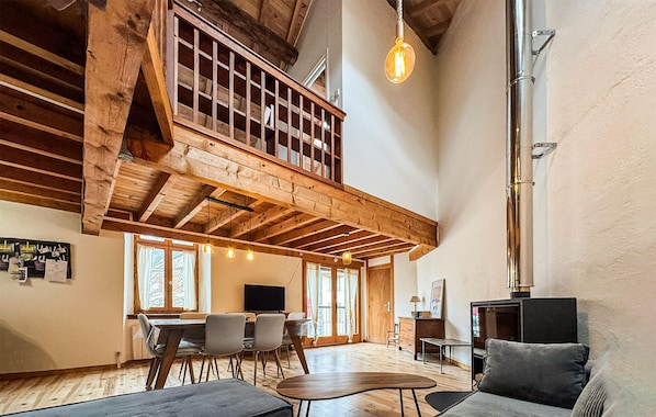 Ein geräumiges Loft mit freiliegenden Holzbalken, einem Essbereich mit Stühlen, einer Couch und einem Kamin.
