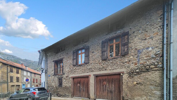 Un b âtiment en pierre doté de trois fenêtres en bois et de deux portes en bois.