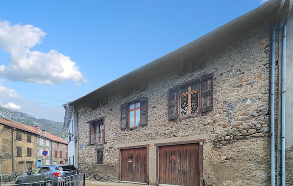 A stone building with three wooden windows and two wooden doors.