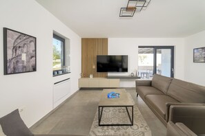 Relax in this stylish living room with a flat-screen TV, comfortable sofa, and a coffee table, offering a view of the outdoor area.