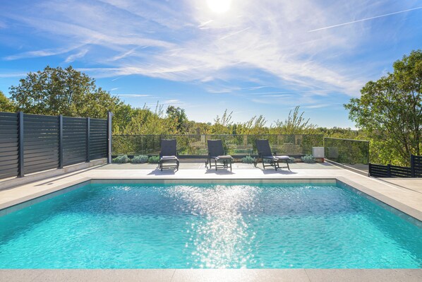 Relax by the pool surrounded by lush greenery and a fence.