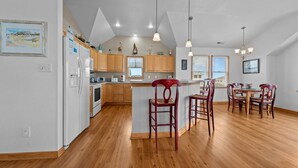 A spacious kitchen with wooden cabinets, a central island, pendant lights, and a dining area with wooden chairs. - 4744- Sandy Beaches, a spacious home in the heart of Kill Devil Hills! (Kitty Hawk)