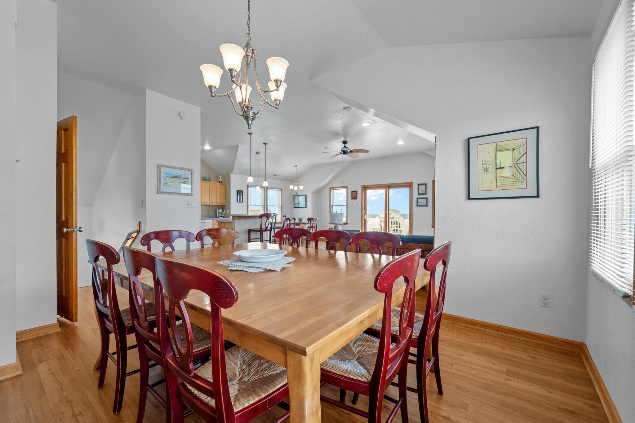A spacious dining area with a wooden table and red chairs, a chandelier, and a view of the kitchen and living area.