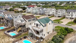 A residential area with multiple two-story houses, each featuring a front yard, a swimming pool, and a covered patio area. - 4744- Sandy Beaches, a spacious home in the heart of Kill Devil Hills! (Kitty Hawk)