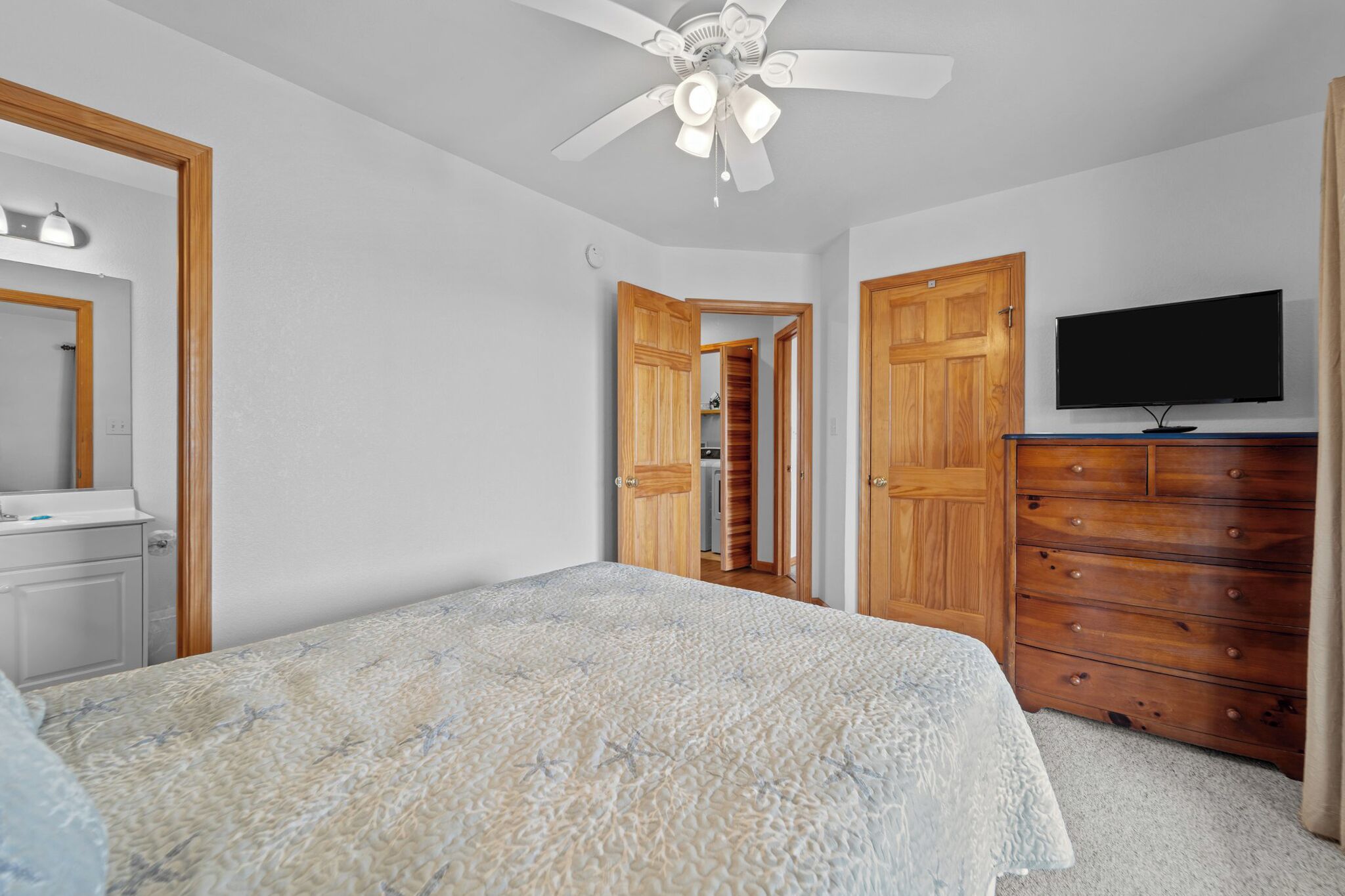 Quarto com cama, ventoinha no teto, cómoda, televisão e guarda-roupa de madeira.