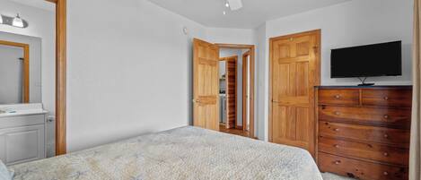 Quarto com cama, ventoinha no teto, cómoda, televisão e guarda-roupa de madeira.