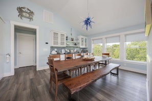 Uma sala de jantar ampla com uma grande mesa de madeira, bancos e um lustre azul pendurado.