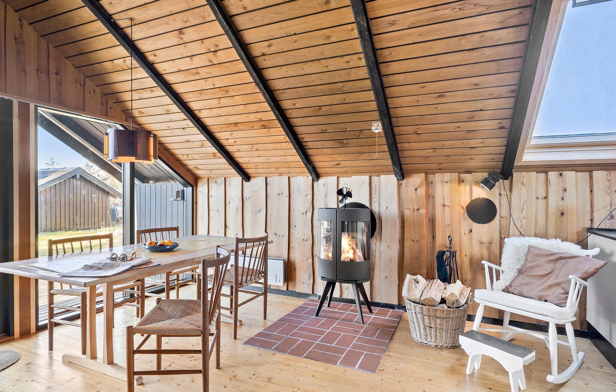 Een gezellig houten cabin interieur met een eethoek, een open haard en een zithoek met een bank en kussens.