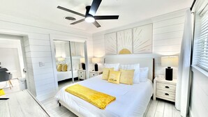 Une chambre à coucher moderne avec un grand lit, des tables de chevet, un ventilateur de plafond et une décoration murale en forme de soleil.
