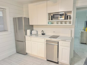 A compact kitchen with white cabinetry, a stainless steel refrigerator, a microwave, and a dishwasher.