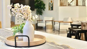 A modern living room with a white sofa, a wooden coffee table, and a white vase with flowers. There are chairs and a staircase in the background. - Zion`s Poolside Paradise (La Verkin)