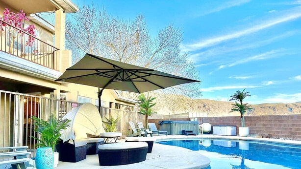 A swimming pool with a curved edge, surrounded by lounge chairs and a covered umbrella. There are potted plants and a barbecue grill in the background. - Zion`s Poolside Paradise (La Verkin)