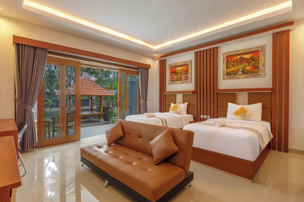 A hotel room with a sofa, two beds, a large window with curtains, and artwork on the walls.