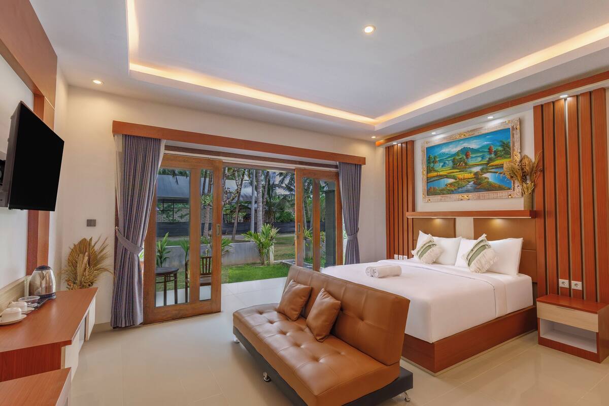 A modern bedroom with a large bed, a sofa, a TV, and a painting on the wall.