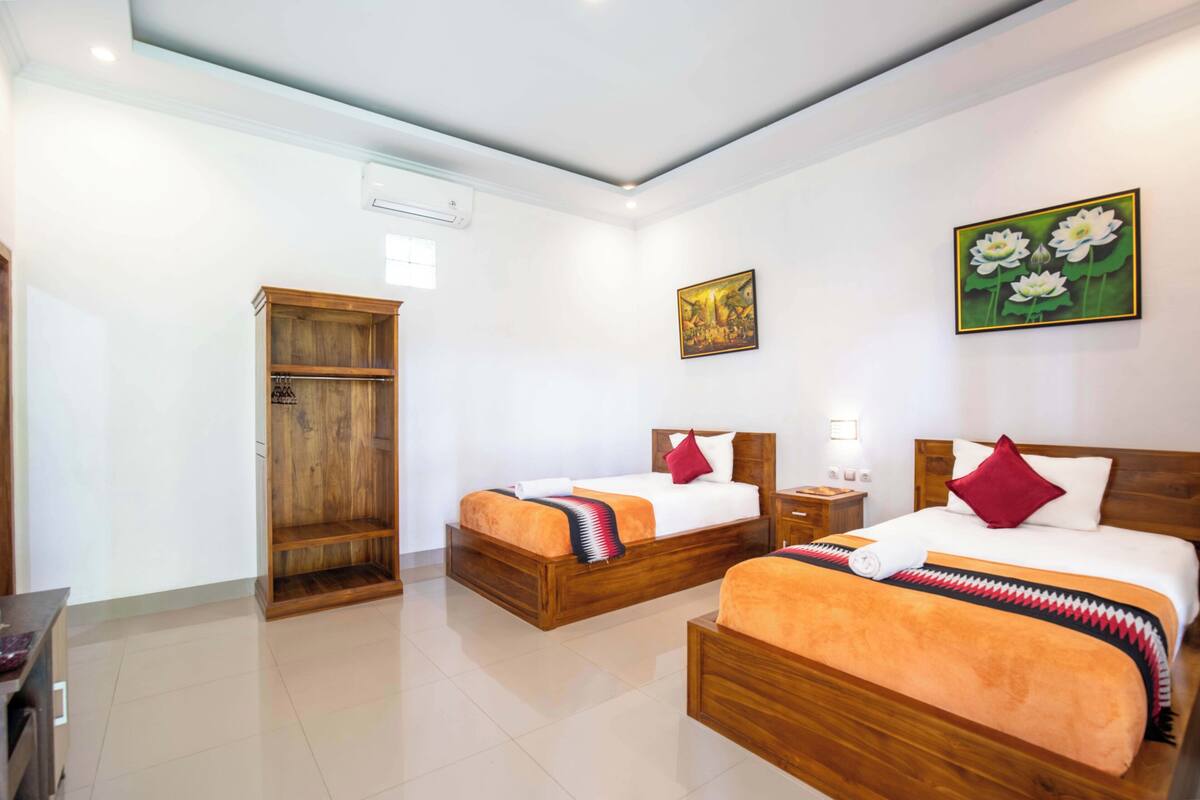 A hotel room with two wooden beds, a wardrobe, and a painting of flowers on the wall.