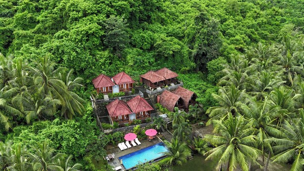 A resort with multiple red-roofed buildings surrounded by dense tropical vegetation and a swimming pool. - Coconut Hill Cottage (Penida Island)