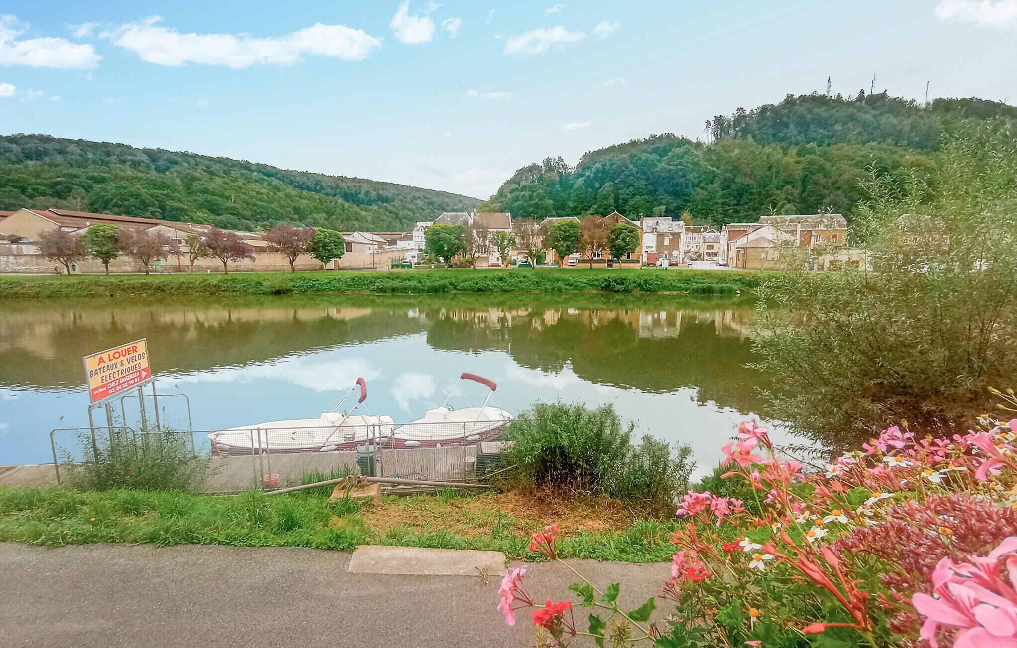 A calm lake with a boat dock, surrounded by greenery and residential buildings.