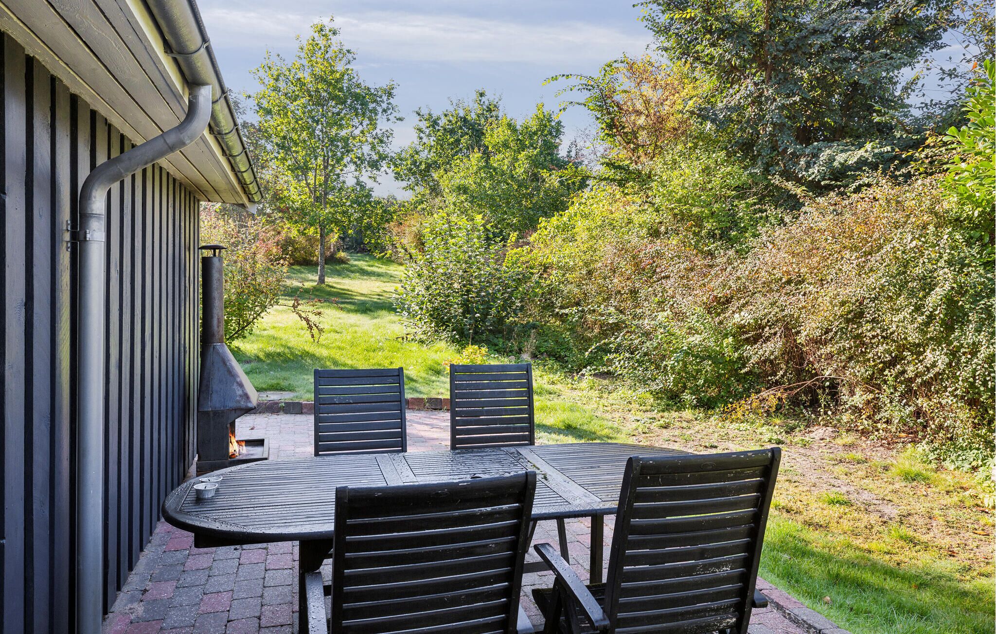 Een terras buiten met een tafel en vier stoelen, omgeven door groen en bomen.