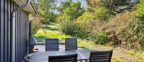Een terras buiten met een tafel en vier stoelen, omgeven door groen en bomen.