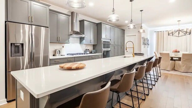 Una cocina moderna con electrodomésticos de acero inoxidable, una encimera blanca y taburetes de bar.