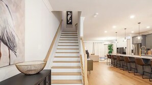 Una cocina moderna con una isla central, una escalera de madera y asientos tipo barra.