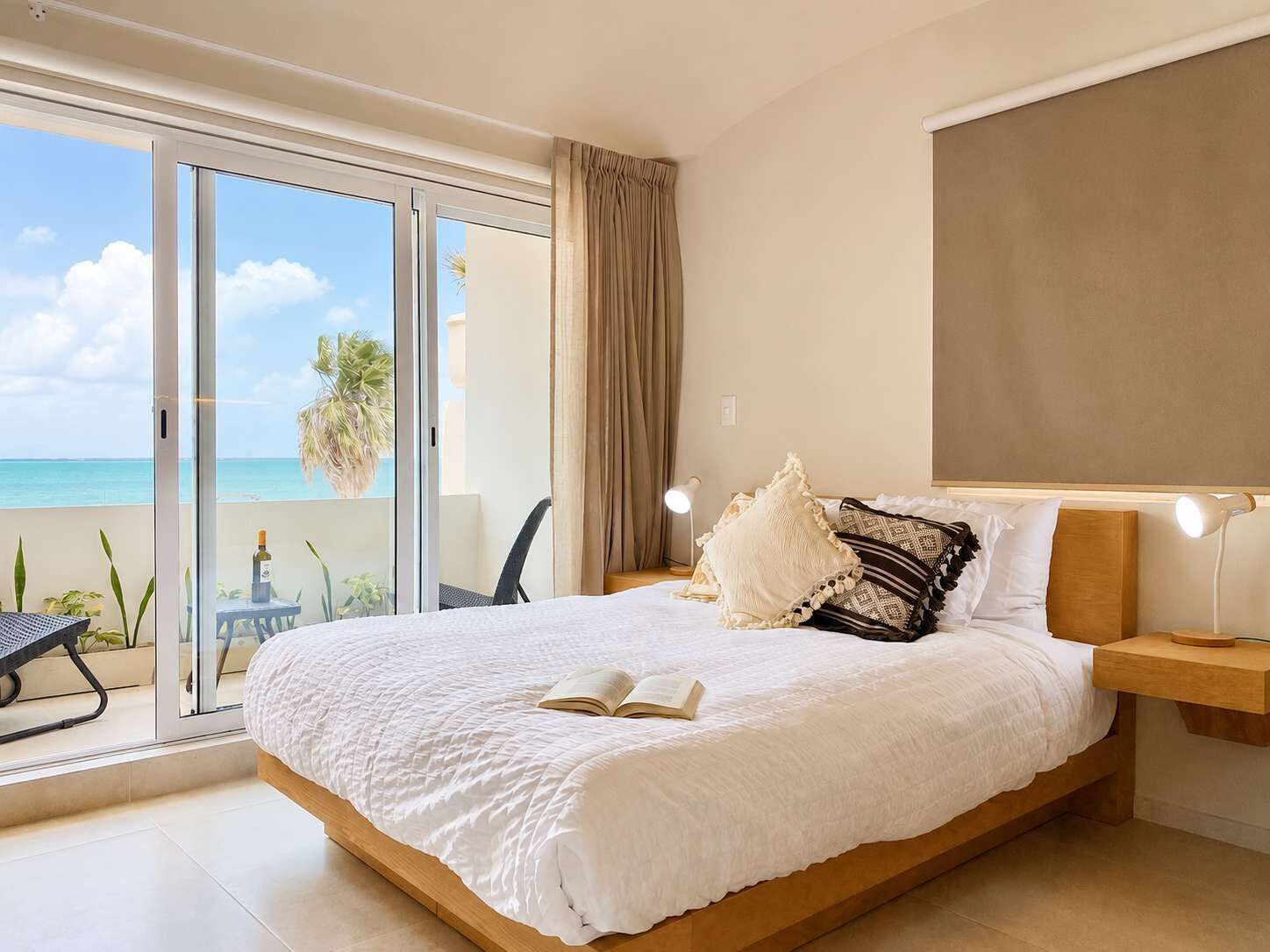 A bedroom with a large bed, a nightstand, a reading lamp, and a view of the ocean through a sliding door.