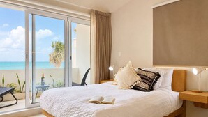 A bedroom with a large bed, a nightstand, a reading lamp, and a view of the ocean through a sliding door. - Studio - Lagoon-View Balcony - Cancun Hotel Zone (Cancún)