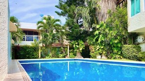 A swimming pool surrounded by lush greenery and a building with a white exterior. - Studio - Lagoon-View Balcony - Cancun Hotel Zone (Cancún)
