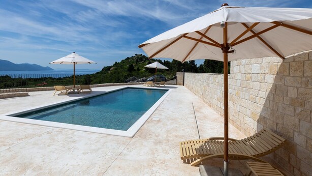 A swimming pool with lounge chairs and umbrellas, surrounded by stone walls and a view of the sea and mountains. - Amazing home in Slivno Ravno with sauna (Slivno Ravno)