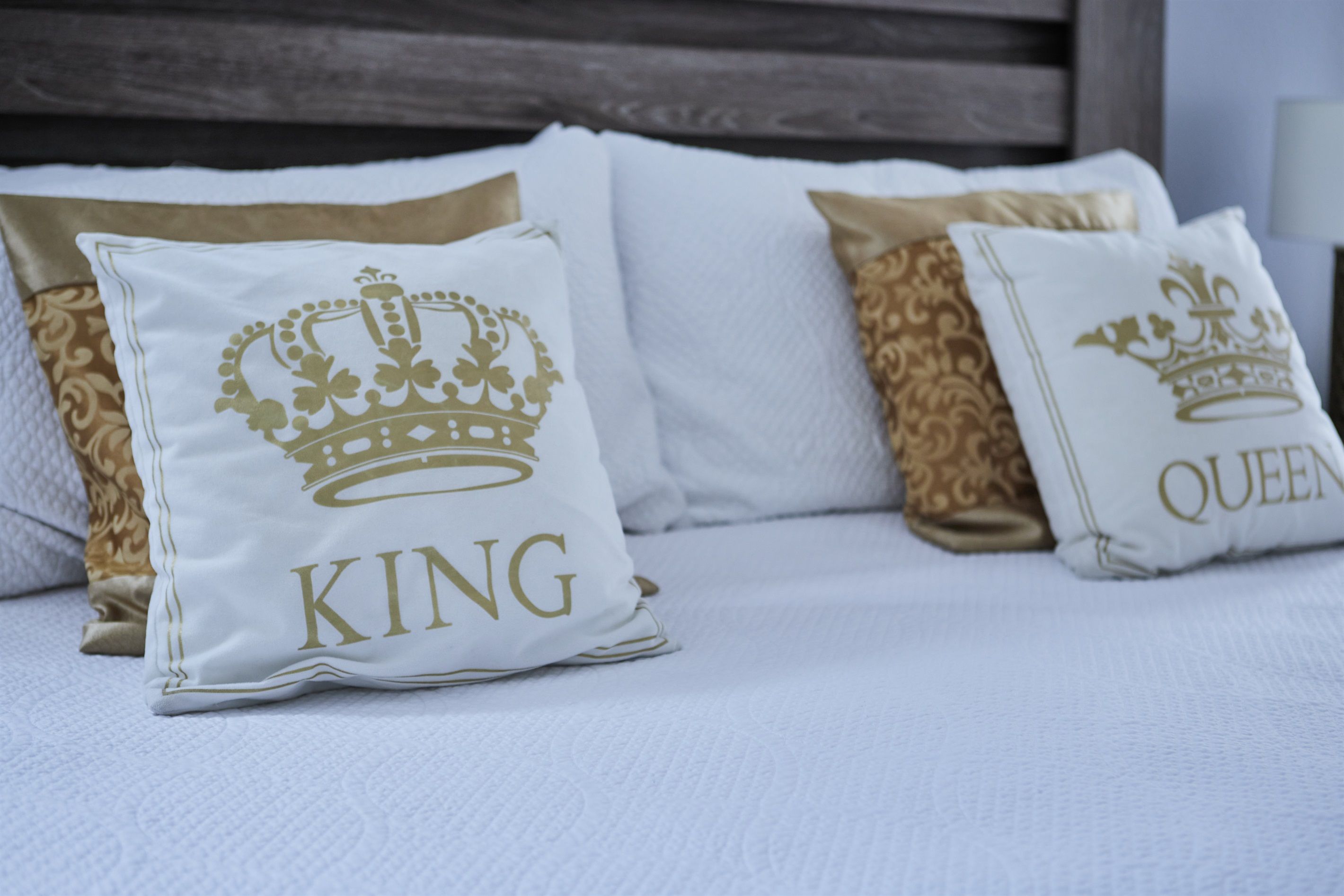 Ein Bett mit drei Kissen, zwei mit "KING" und ein Kissen mit "QUEEN" aufgestickt.