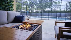 A poolside area with a fire feature, a sofa, and a chair. - Luxury Disney Getaway with Pool (Davenport)