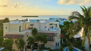 A coastal residential area with multiple buildings, some with rooftop terraces, and a view of the sea and an island in the distance. - 4BR House | Hotel Zone | Beach & 3 Pools (Cancún)