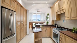 A modern kitchen with wooden cabinets, stainless steel appliances, a central island, and a view to the outside. - 4BR House | Hotel Zone | Beach & 3 Pools (Cancún)