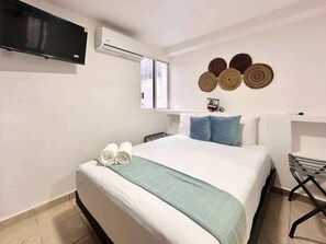 A hotel room with a bed, a TV, an air conditioner, a window, and wall decor. - Modern Studio - Wi-Fi, A/C & Rooftop Terrace (Cancún)