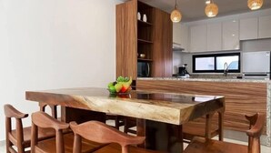 A modern kitchen with wooden cabinetry, a marble countertop, and a dining area with wooden chairs. - 4BR House · Sleeps 12 · Shared Pool · Playa (Playa del Carmen)